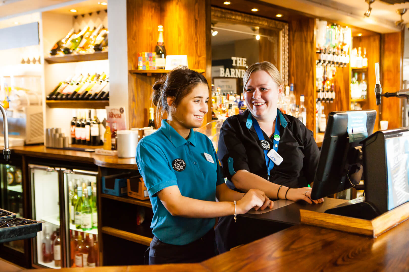 An assistant manager with a staff member smiling as they operate a till