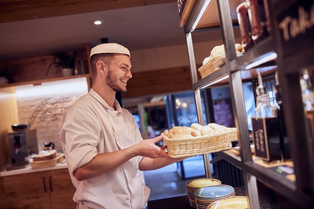 A harvester kitchen assistant smiling while carrying a bread basket