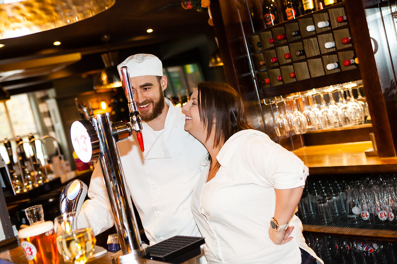 man in chef whites laughing with a women behind the bar