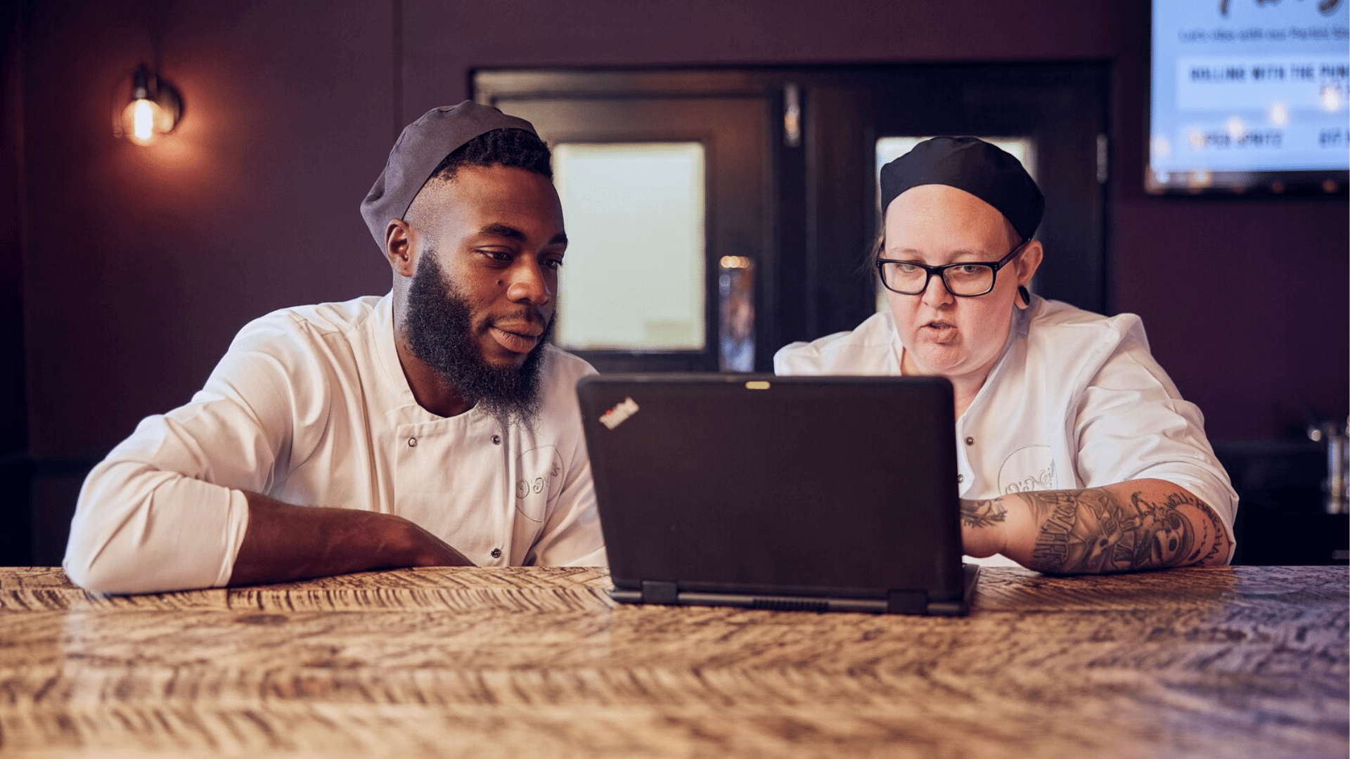 A chef and chef apprentice working through some training on the laptop 