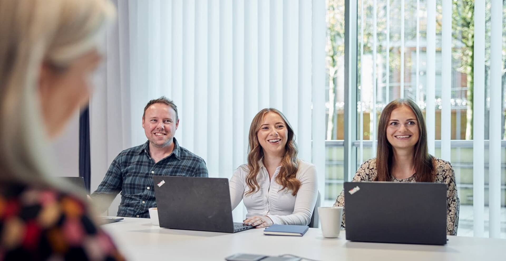 image of graduate and team in a meeting smiling with laptops on desk 