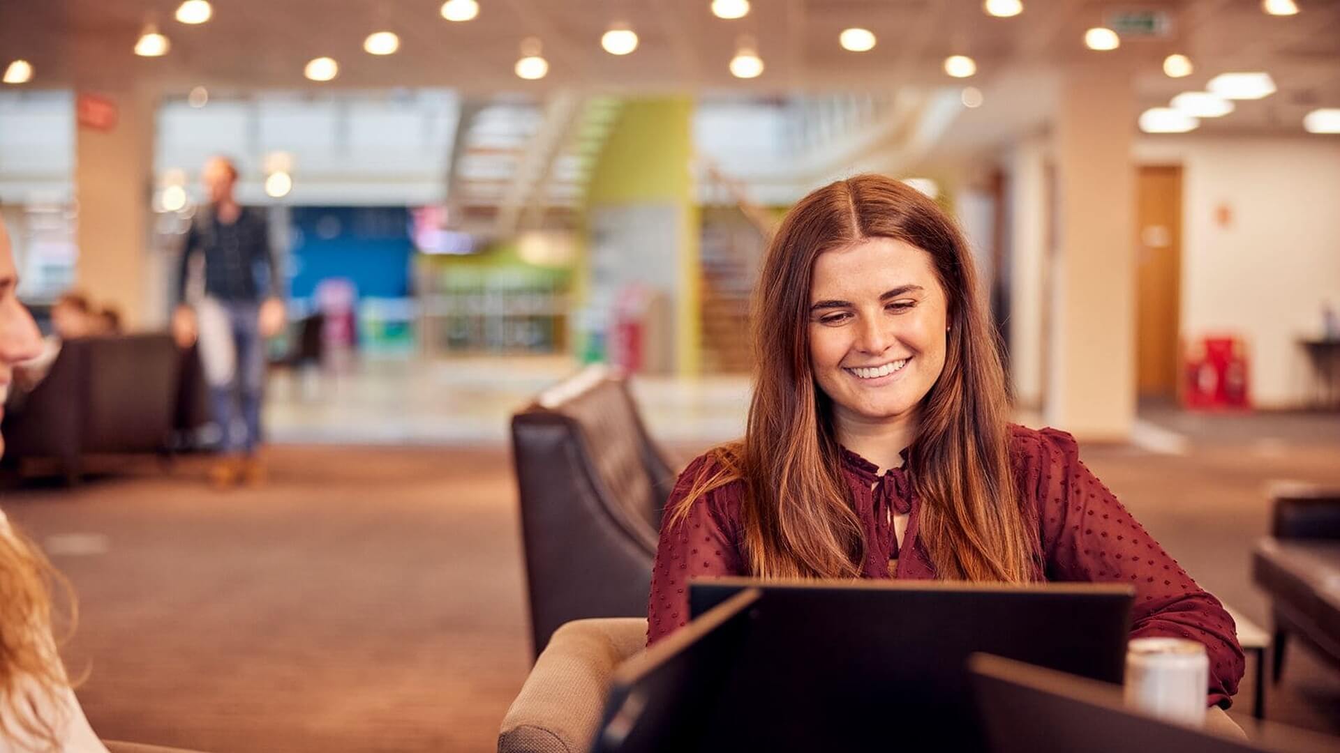 apprentice sitting on sofa working on laptop smiling 