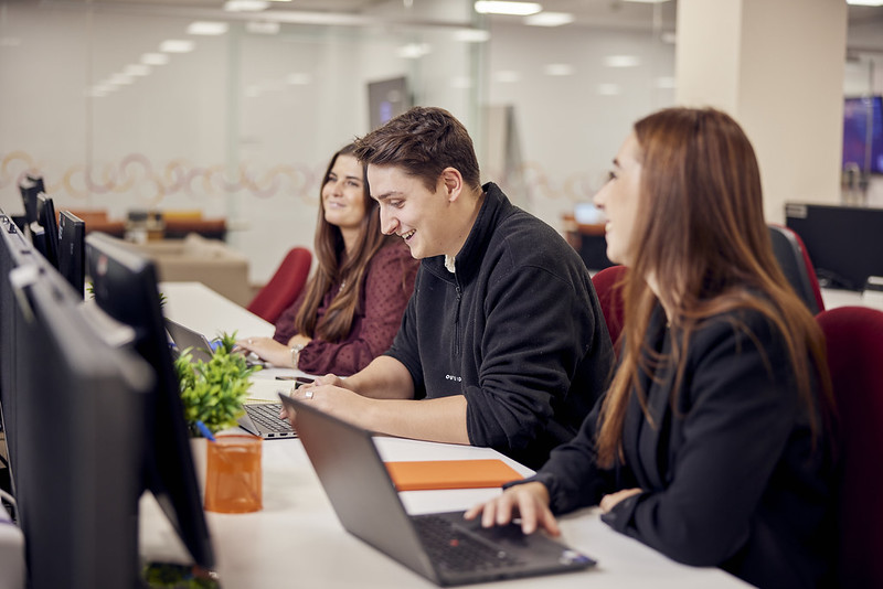 three people sitting at a line of computers laughing