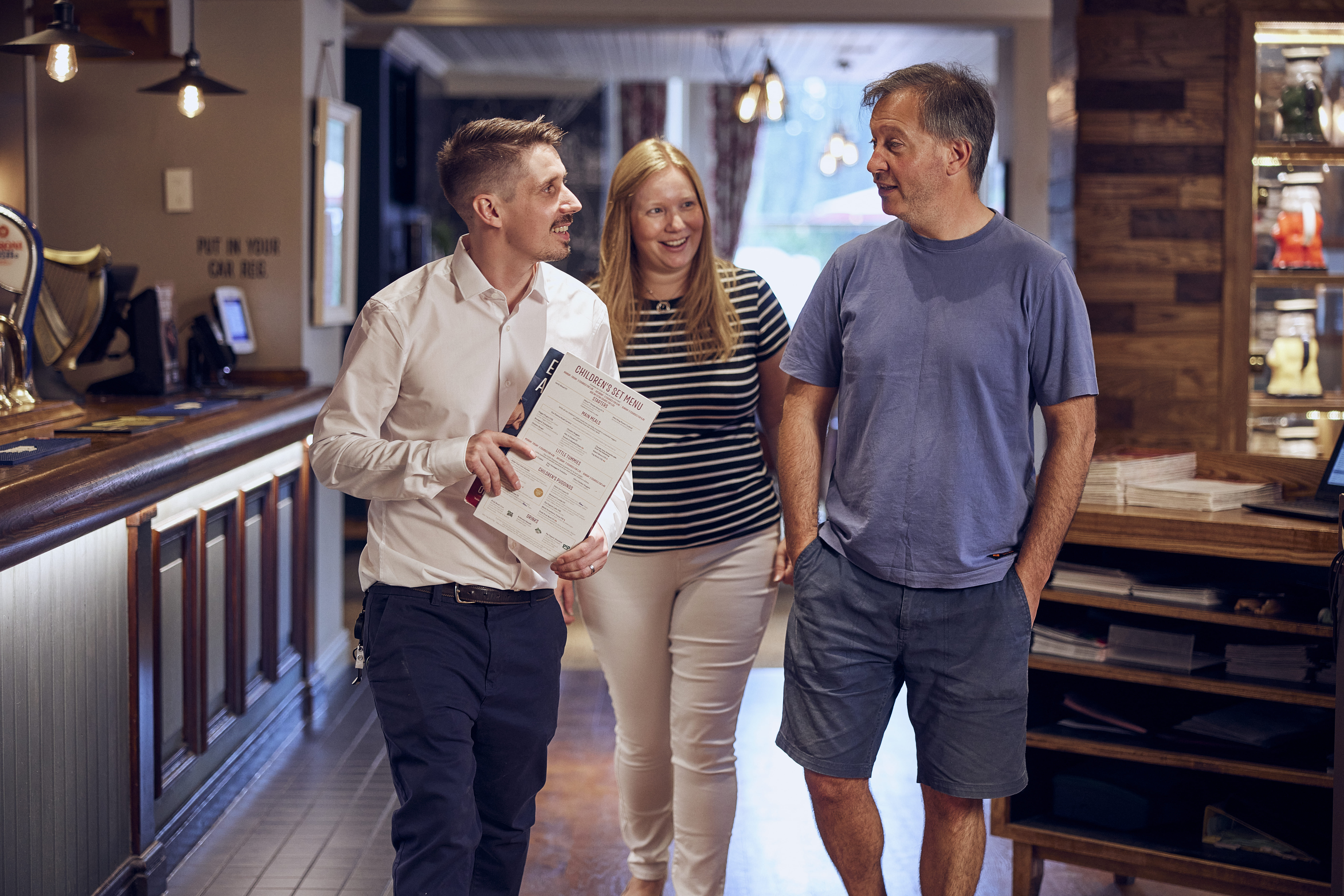 Assistant manager seating two customers smiling and holding menu 