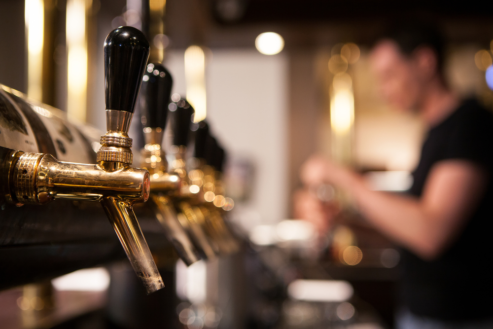 Close up of beer taps in a row with male bar staff serving in a blurred background