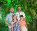 There are four people in the image, a family posing together next to a green palm tree.