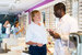 woman in white top talking to man in a white optometrist's jacket holding red glasses