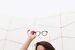 woman lifting her glasses above her head against white background with lines 