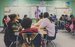 Children sitting in a classroom listening to a teacher stood up