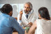 man in white lab coat holding glasses and talking to a man and woman