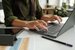 A woman at a table typing at a laptop.