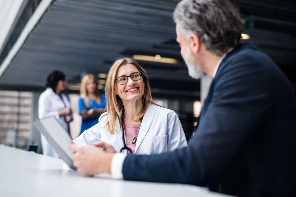 woman in white lab coat and stethoscope talking to a man looking at a notepad