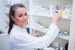 Image of a young female clinical pharmacist smiling at the camera whilst reaching for a bottle of medicine from the shelf