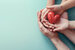 hands holding a red heart against a blue backdrop