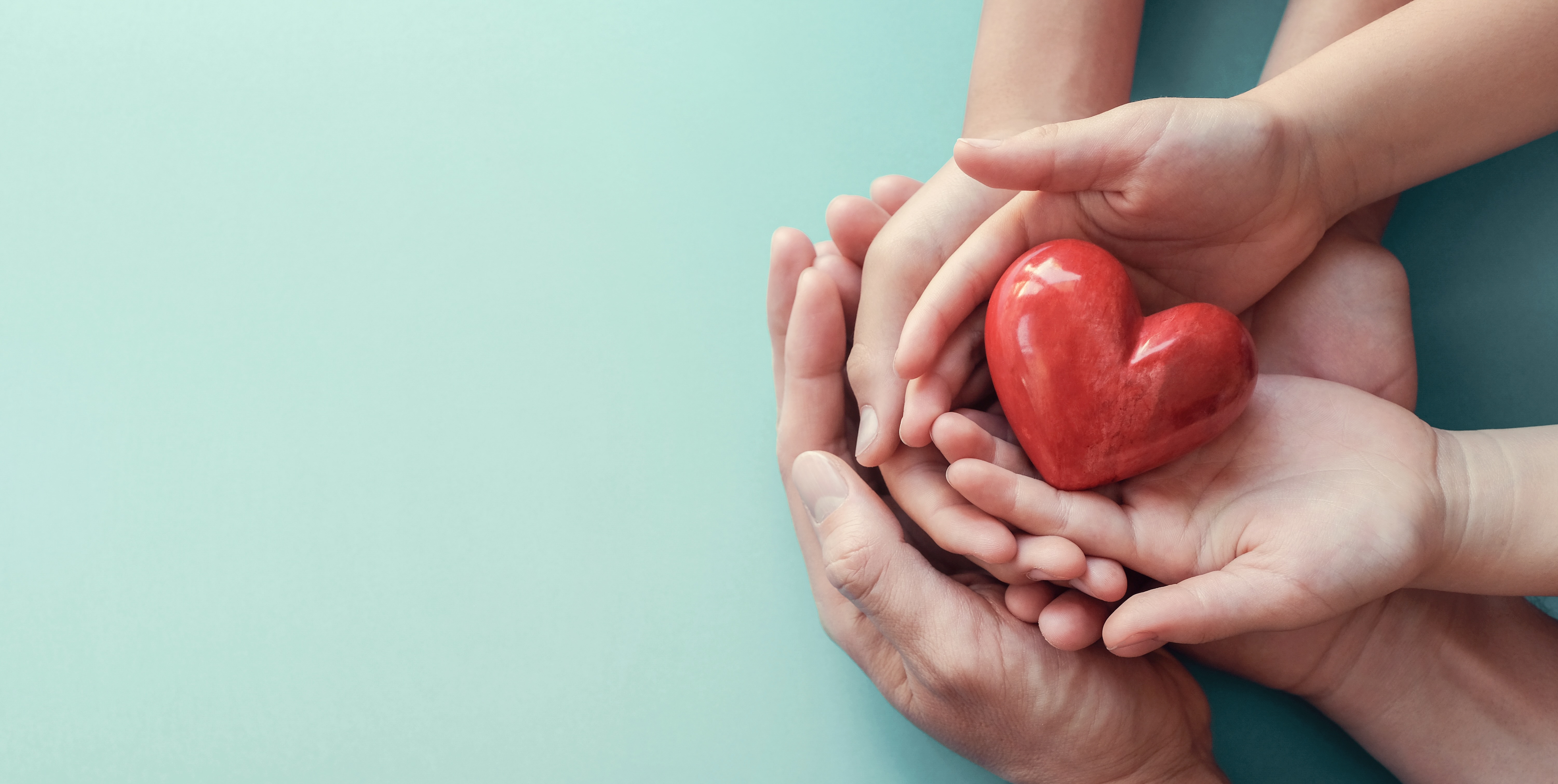 hands holding a red heart against a blue backdrop