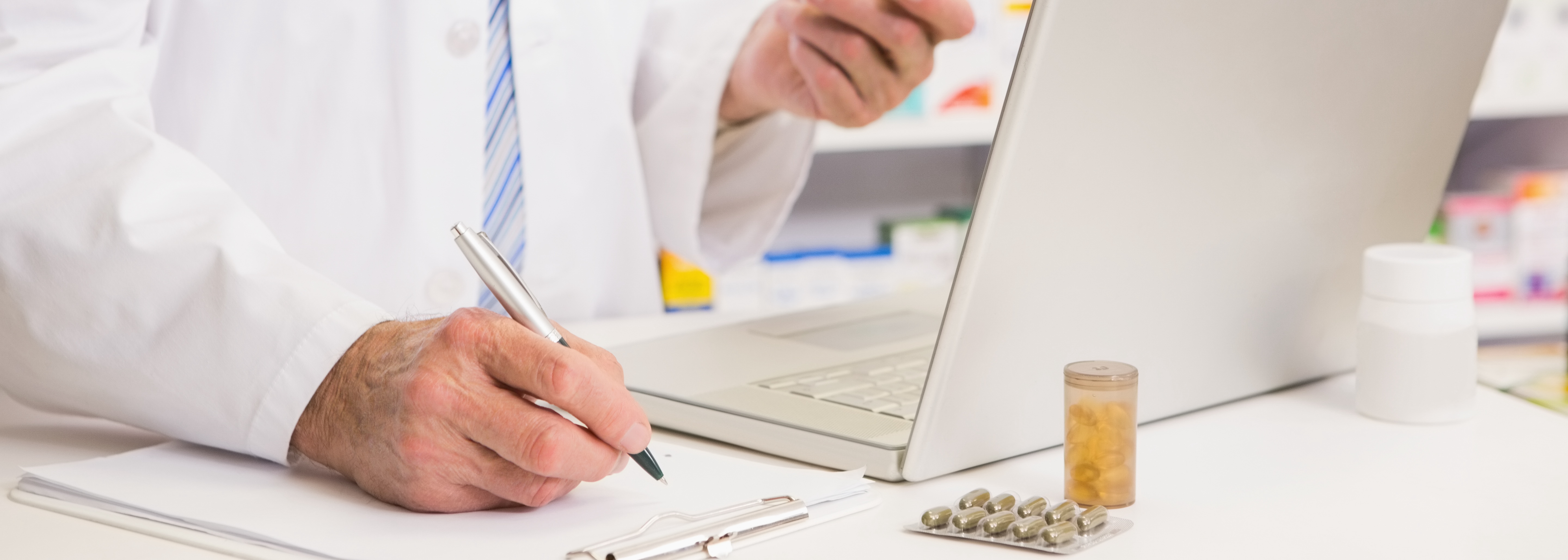 Pharmacist writing on clipboard and holding medication in the pharmacy