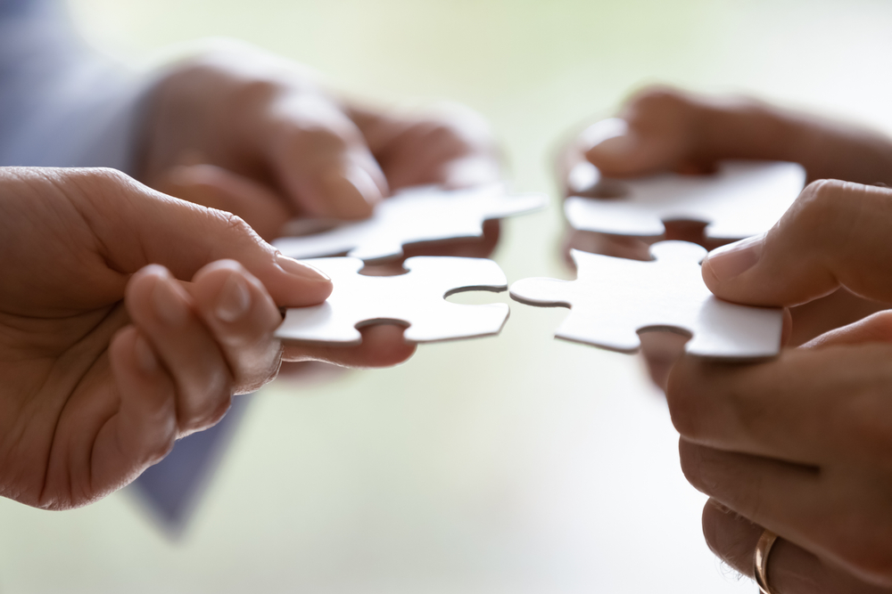 four hands, each holding a piece of a jigsaw, placing the pieces together.