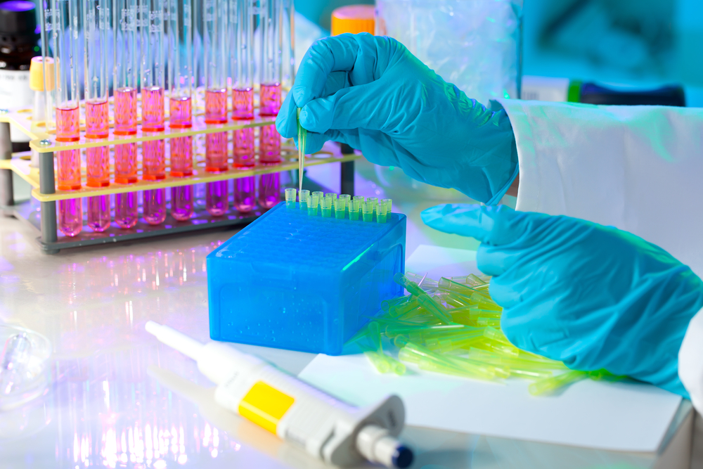 gloved hand holding pipette and dropping a solution into test tubes