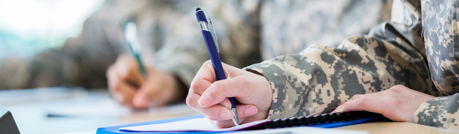 Person in army clothing writing on paper with a pen