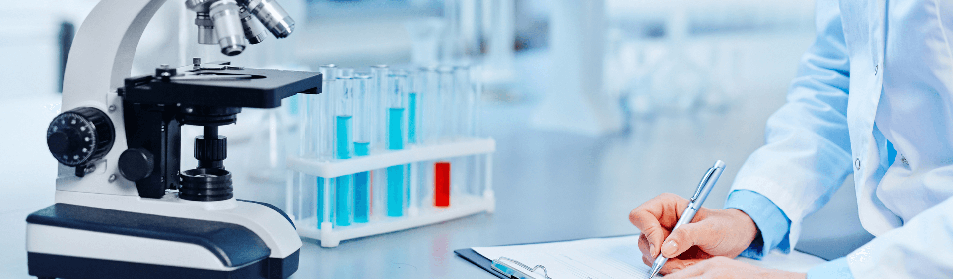 Scientist in lab writing on clipboard, next to microscope