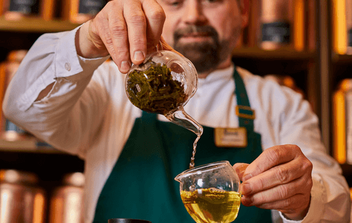 a man with a teapot pouring tea into a glass cup