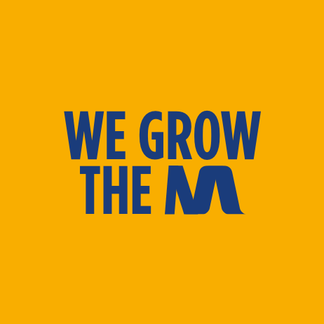 part 2 of the company manifesto that reads we grow the m written in a bold, blue font across an orange backdrop