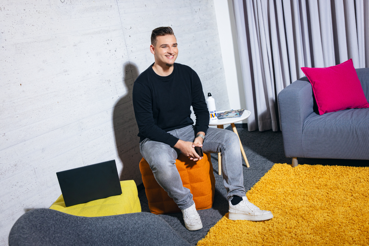 a man in a modern office space sitting over a stool and smiling