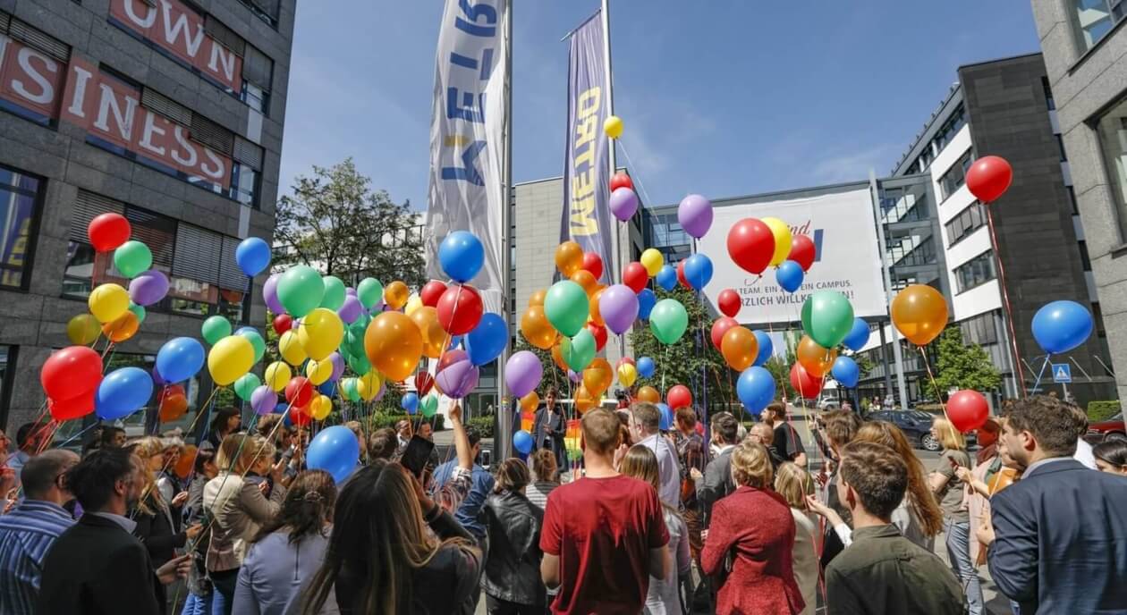 a parade with people carrying multicolored balloons at the office premises with company flags 