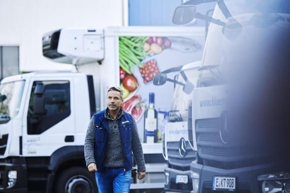 a man wearing a company branded jacket walking between cargo trucks 