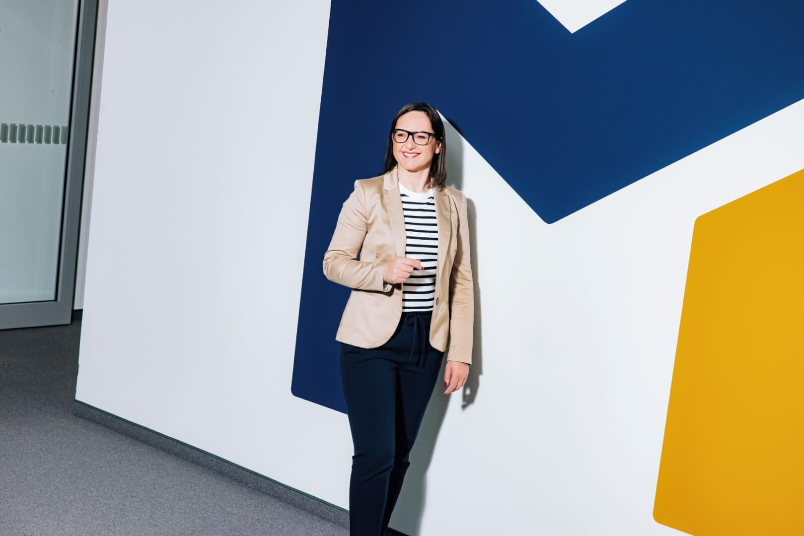 a working professional standing against a wall showing the company logo, a bold M