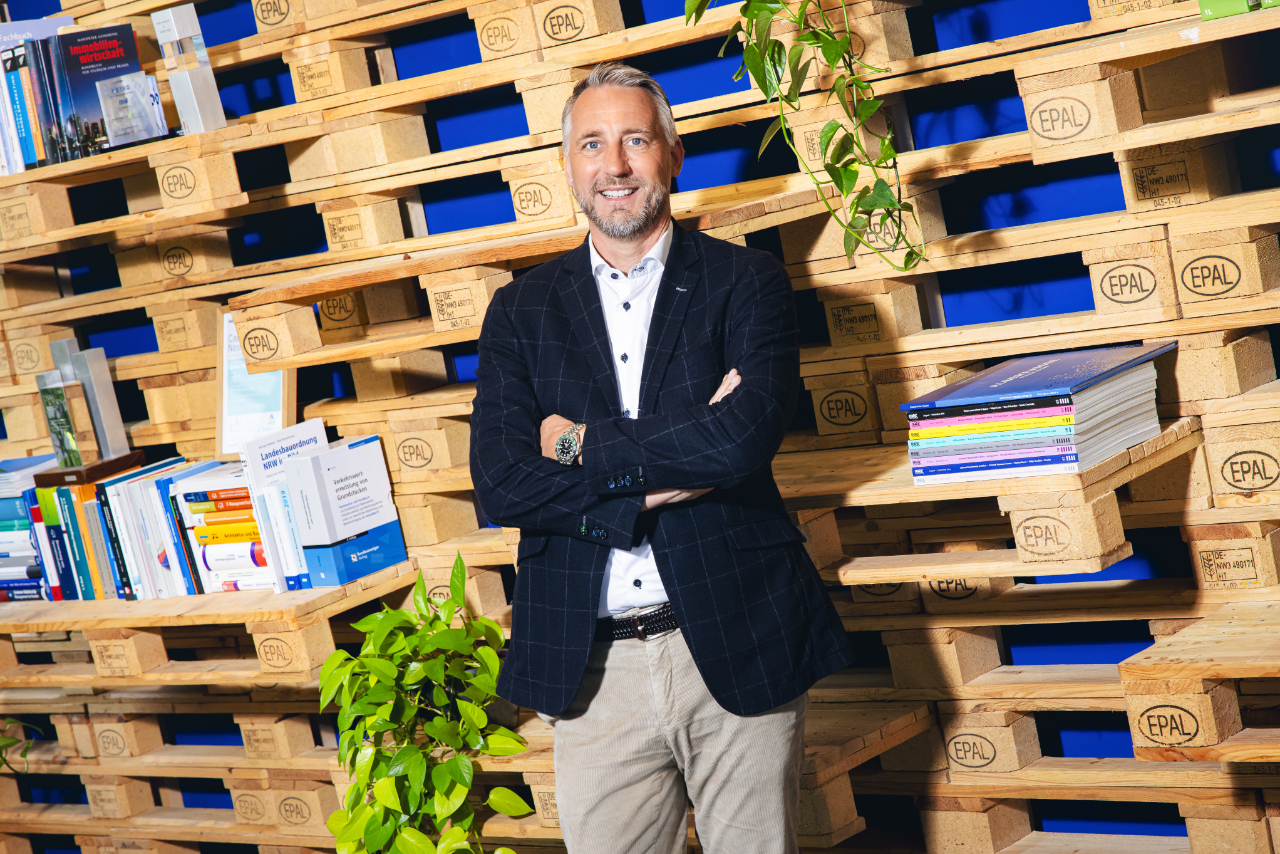a working professional standing across a bookshelf and smiling