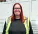 Image of Sheila, a distribution manager at Travis Perkins wearing a high-visibility vest with red hair and glasses