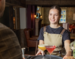 A girl with hair tied back and work apron on, serving drinks to a customer in a pub