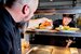 A kitchen assistant passing food orders to a waiter.