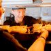 A smiling chef passing cooked meals to waiting staff