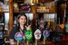 A smiling woman behind a bar pulling a pint of beer.