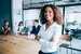 An image of a lady smiling in an office in front of her coworkers.