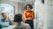 A woman in an orange blouse stood in front of a whiteboard of ideas.