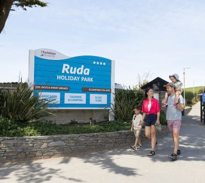 Ruda Holiday Park sign and family walking past smiling