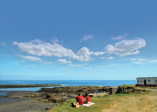 mage of a couple sat on the ground, looking out at the sea