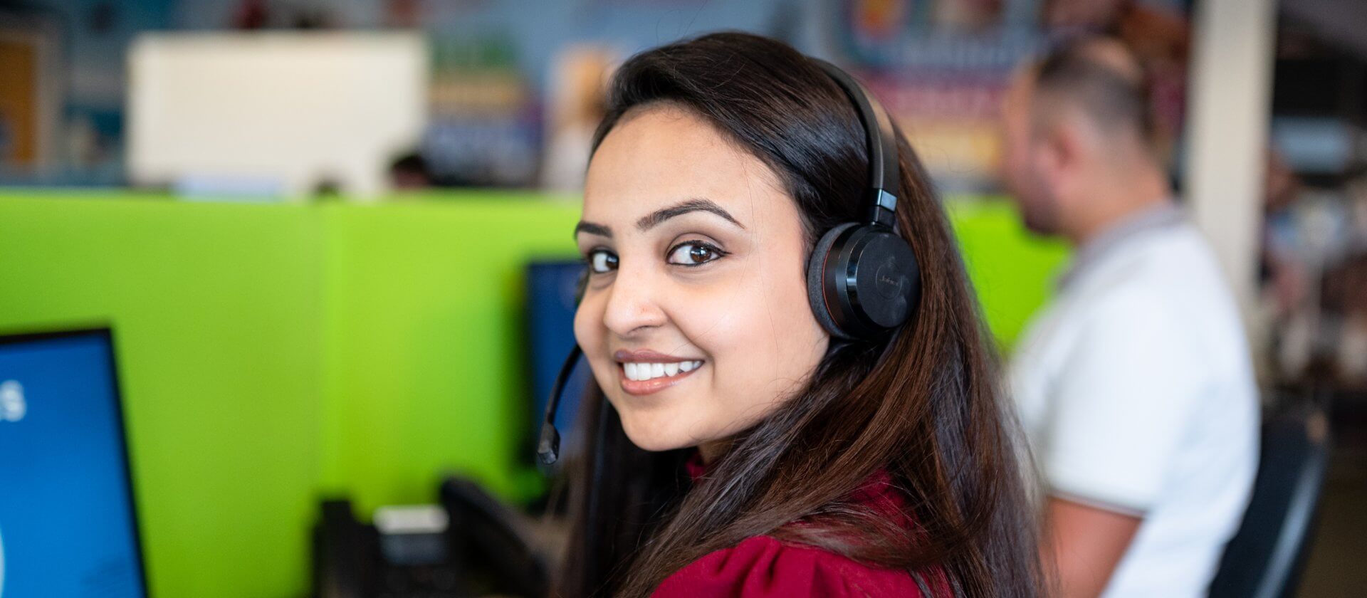 Image of woman looking over her shoulder and smiling, with a head set on in a contact centre