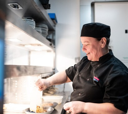 Image of chef at the pass serving up a dish