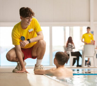 Image of lifeguard crouched down speaking to a child who is in a swimming pool