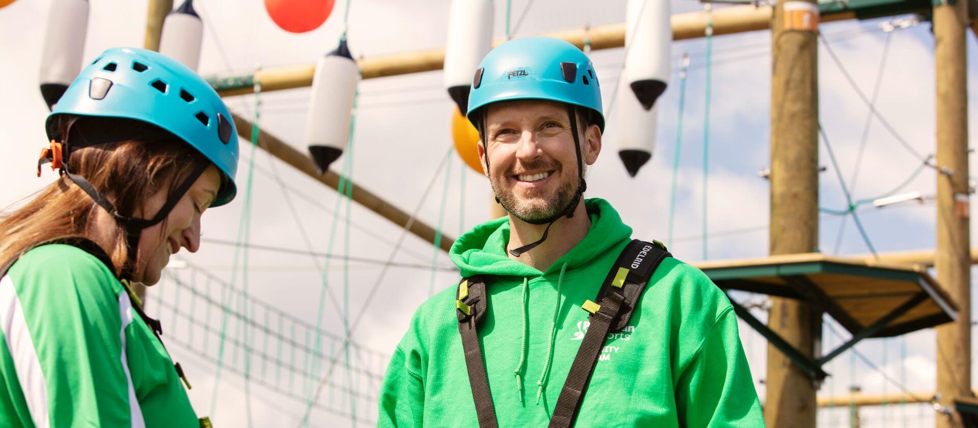 Image of two colleagues in hard hats smiling while on the high ropes course