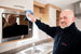 A man in a kitchen cleaning a microwave door with a blue cloth.