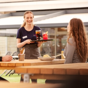 image of a waitress carrying drinks to customers sat on a wooden bench