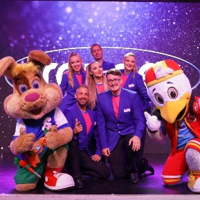 Group of performers in purple blazers posing on stage