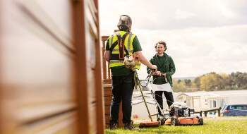 Image of a man mowing the lawn in green high vis speaking with another man