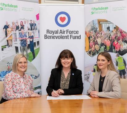 Image of three women sat at a table signing a document while smiling