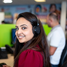 image of a woman in a call centre, wearing headphones, looking over her shoulder smiling
